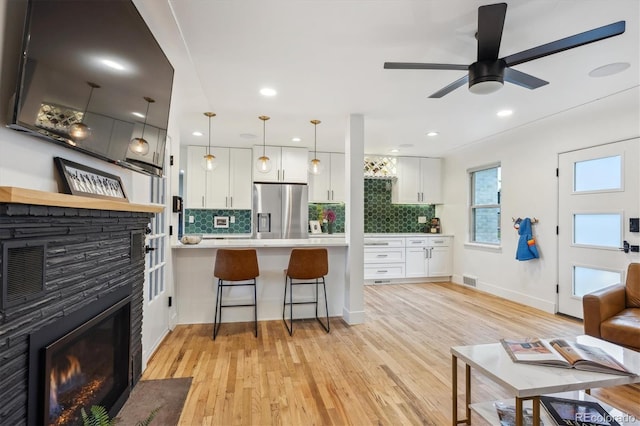 kitchen featuring stainless steel fridge with ice dispenser, light countertops, a stone fireplace, light wood finished floors, and recessed lighting
