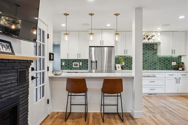 kitchen featuring stainless steel refrigerator with ice dispenser, light countertops, white cabinets, a breakfast bar, and recessed lighting