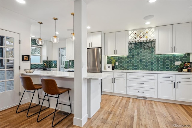 kitchen with freestanding refrigerator, white cabinets, decorative backsplash, a kitchen breakfast bar, and recessed lighting