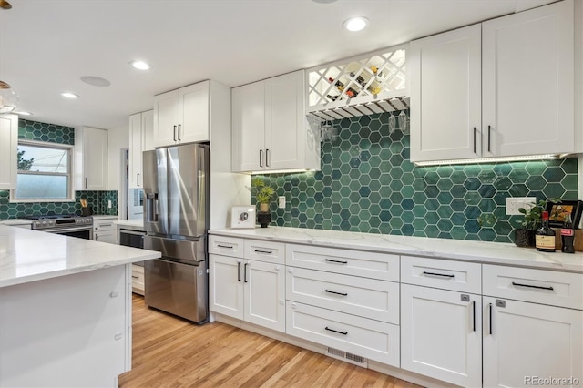 kitchen featuring appliances with stainless steel finishes, white cabinets, backsplash, light wood-style floors, and light stone counters