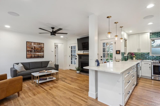 kitchen with appliances with stainless steel finishes, a sink, open floor plan, white cabinetry, and a fireplace