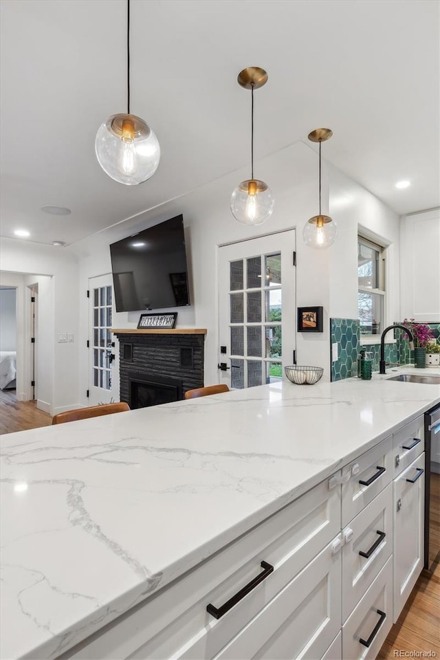 kitchen featuring a sink, white cabinets, light stone countertops, and hanging light fixtures