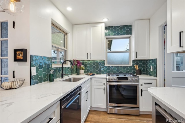 kitchen featuring stainless steel gas stove, a sink, white cabinetry, light stone counters, and backsplash