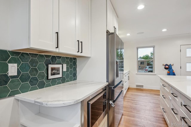 kitchen with appliances with stainless steel finishes, white cabinetry, light stone countertops, light wood-style flooring, and tasteful backsplash