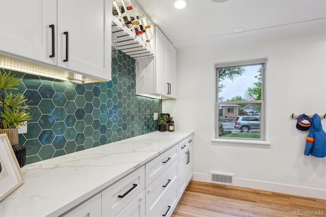 kitchen with baseboards, light wood-style floors, white cabinetry, decorative backsplash, and light stone counters