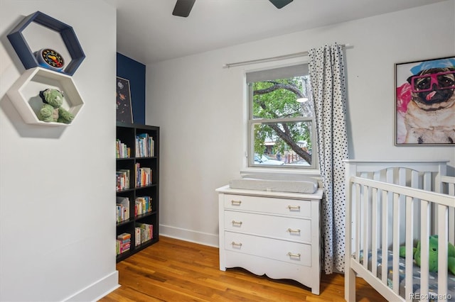 bedroom featuring baseboards, light wood-type flooring, a ceiling fan, and a crib