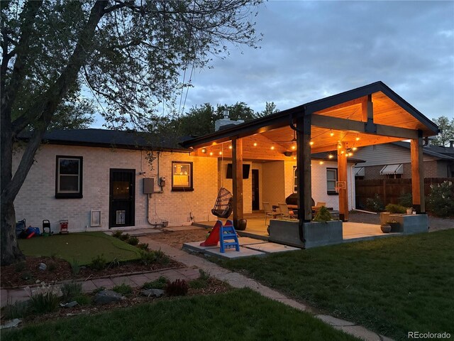 back of house featuring a patio, a lawn, and brick siding
