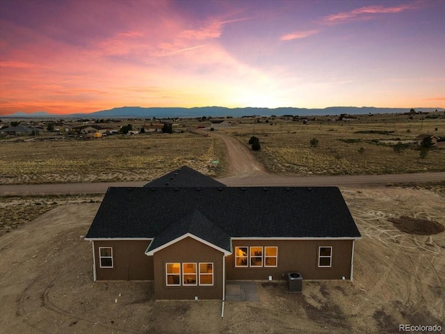 back house at dusk with central AC, a patio area, and a mountain view