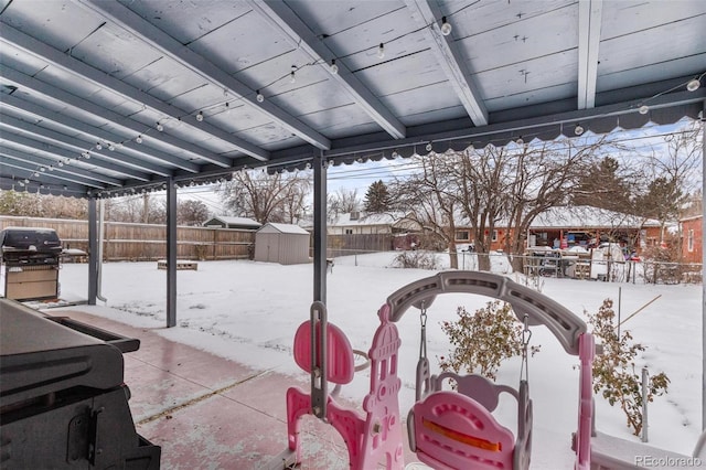 snow covered patio with a grill and a storage unit