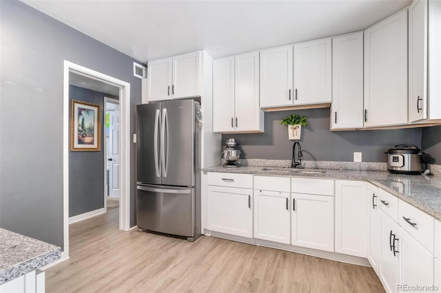 kitchen with white cabinetry, stainless steel fridge, sink, and light hardwood / wood-style flooring