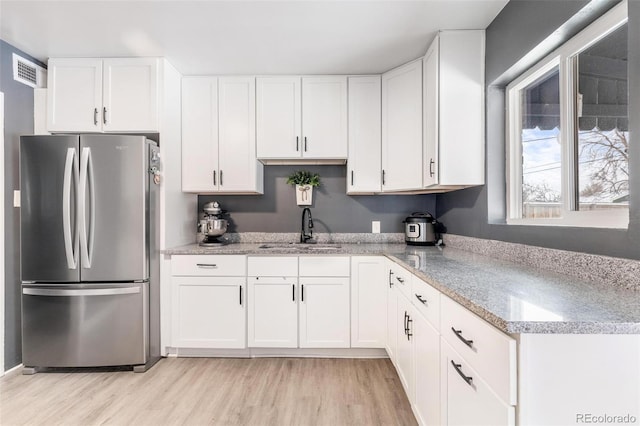 kitchen featuring white cabinetry, sink, light hardwood / wood-style flooring, and stainless steel refrigerator