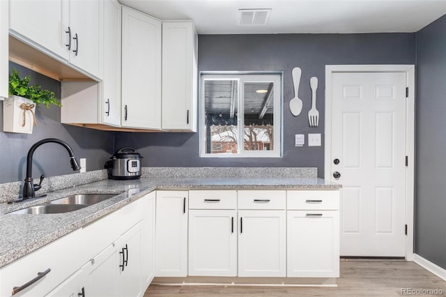 kitchen featuring white cabinetry, sink, light stone counters, and light hardwood / wood-style flooring