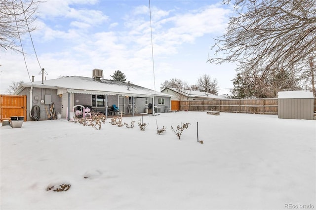 snow covered back of property featuring cooling unit and a storage shed