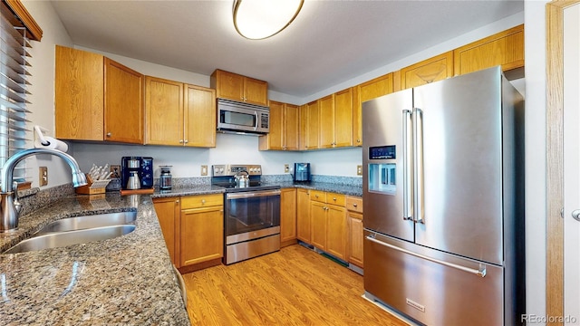 kitchen with stainless steel appliances, sink, dark stone counters, and light hardwood / wood-style flooring