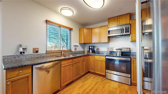 kitchen with stainless steel appliances, dark stone countertops, sink, and light hardwood / wood-style flooring