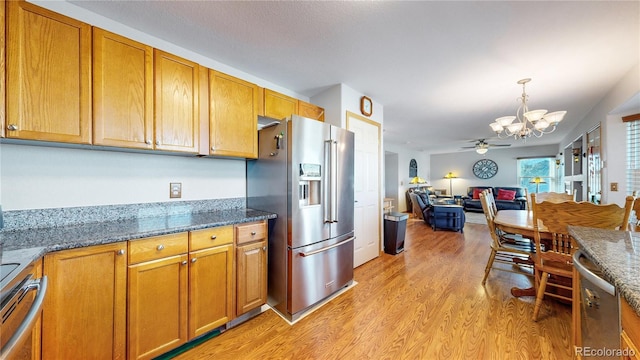 kitchen featuring light hardwood / wood-style flooring, pendant lighting, ceiling fan with notable chandelier, appliances with stainless steel finishes, and dark stone countertops