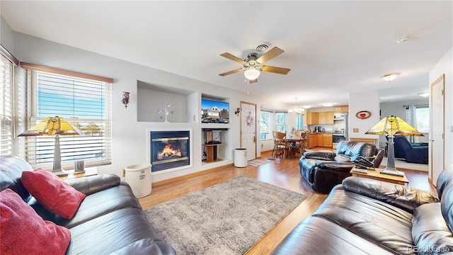 living room featuring ceiling fan with notable chandelier and light wood-type flooring