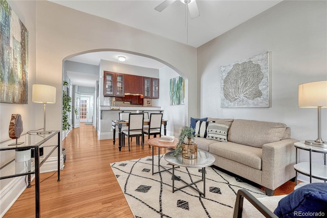 living room with light wood-style floors, arched walkways, and a ceiling fan