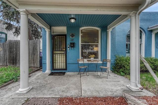 property entrance featuring fence, covered porch, and stucco siding