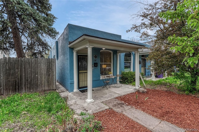 shotgun-style home featuring covered porch, fence, and stucco siding