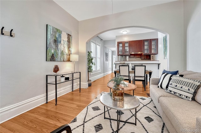 living room with light wood-style floors, arched walkways, and baseboards