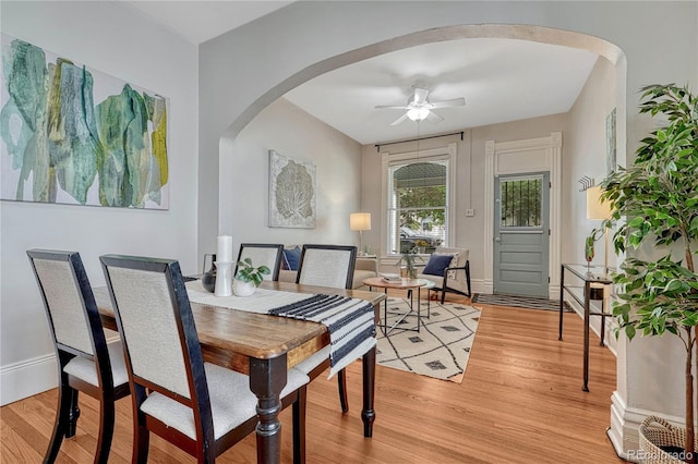 dining room featuring arched walkways, baseboards, a ceiling fan, and light wood finished floors