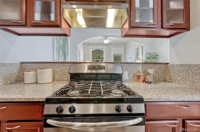 kitchen featuring glass insert cabinets, light countertops, arched walkways, backsplash, and gas stove