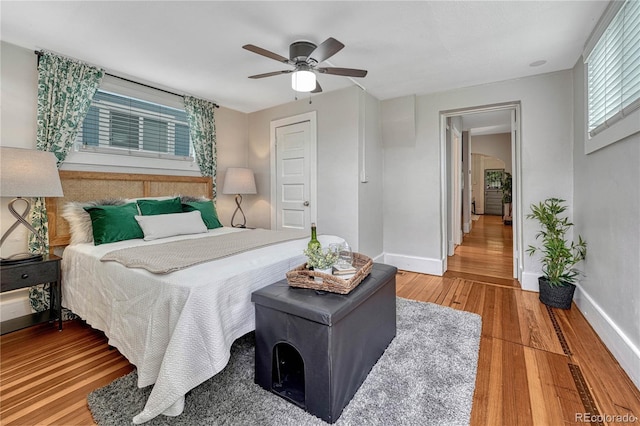 bedroom featuring ceiling fan, baseboards, multiple windows, and wood finished floors