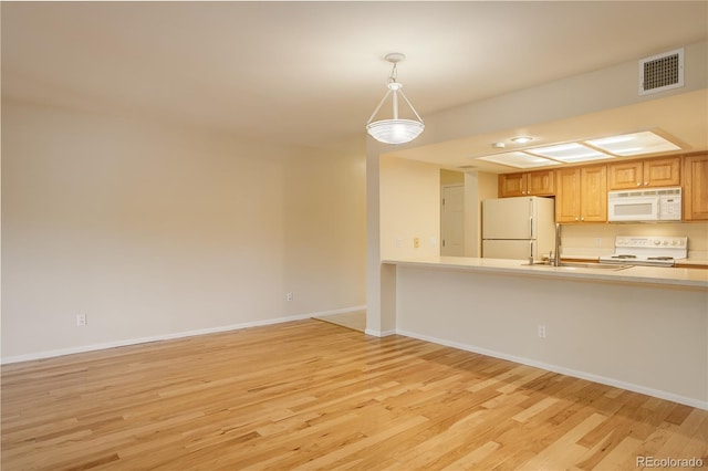 kitchen with pendant lighting, sink, white appliances, and light wood-type flooring