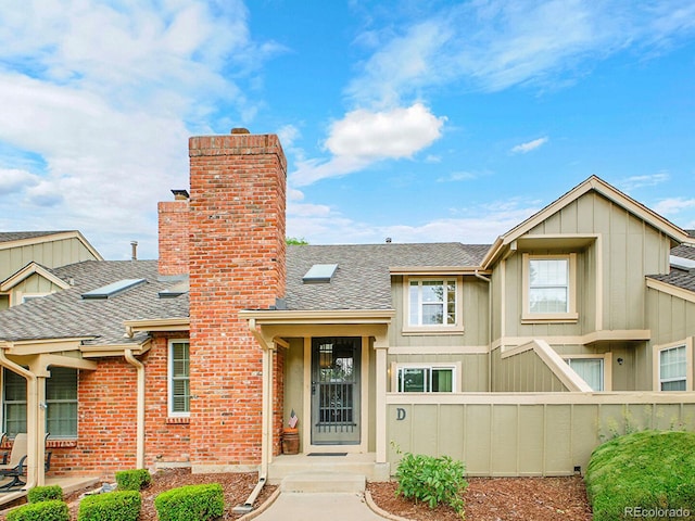7781 S Curtice Dr Unit D, Littleton, CO 80120 - view of front of house with a shingled roof, a chimney, board and batten siding, and brick siding