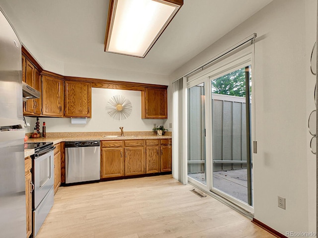 7781 S Curtice Dr Unit D, Littleton, CO 80120 - kitchen featuring stainless steel appliances, brown cabinetry, under cabinet range hood, light wood-type flooring, and light countertops
