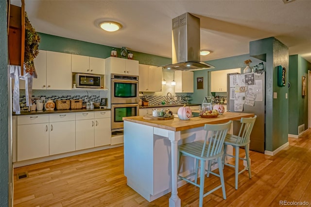 kitchen with light hardwood / wood-style flooring, island range hood, appliances with stainless steel finishes, a breakfast bar area, and white cabinets