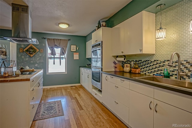 kitchen featuring white cabinetry, light hardwood / wood-style flooring, decorative light fixtures, exhaust hood, and sink