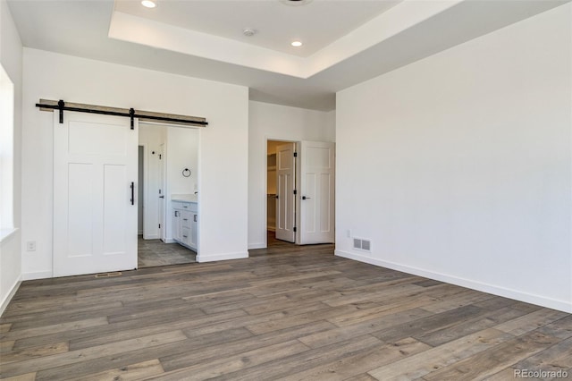 16990 Early Light Dr, Colorado Springs, CO 80908 - unfurnished bedroom with a barn door, wood finished floors, and a tray ceiling