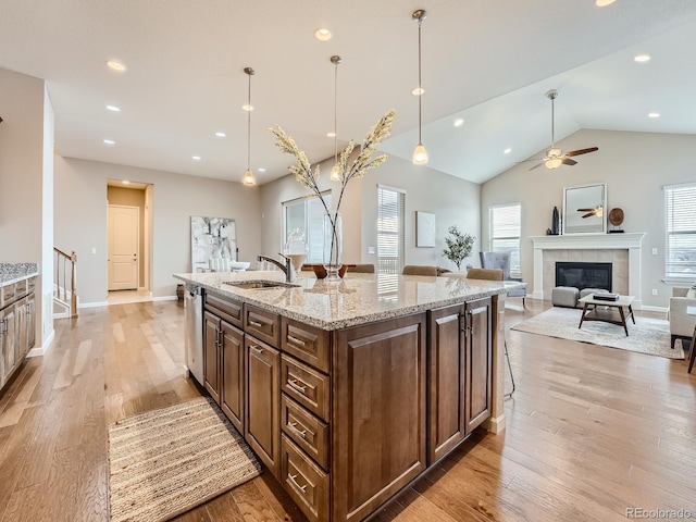 kitchen featuring sink, light stone counters, a center island with sink, decorative light fixtures, and stainless steel dishwasher