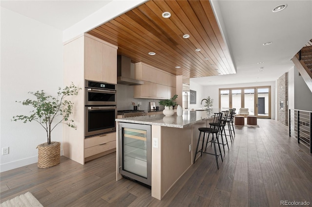 kitchen with wine cooler, wooden ceiling, wall chimney range hood, a center island with sink, and stainless steel appliances