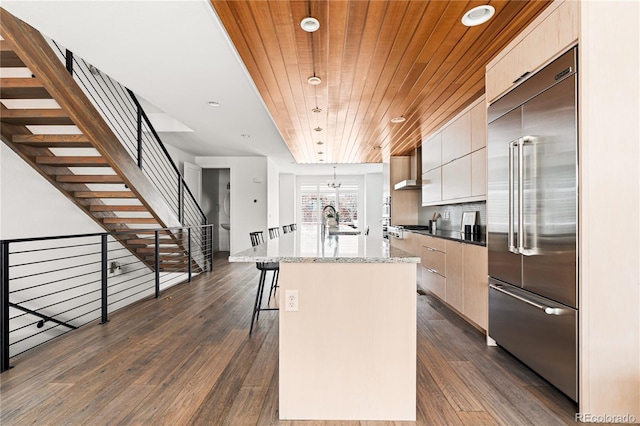 kitchen with hanging light fixtures, appliances with stainless steel finishes, dark wood-type flooring, wood ceiling, and a kitchen island with sink