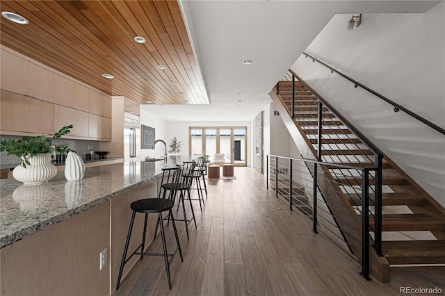 kitchen with sink, dark wood-type flooring, light stone counters, wooden ceiling, and a breakfast bar