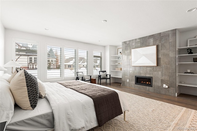 bedroom with a tiled fireplace and dark hardwood / wood-style flooring