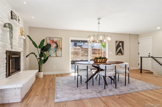 dining area featuring a large fireplace, a notable chandelier, and light wood-type flooring