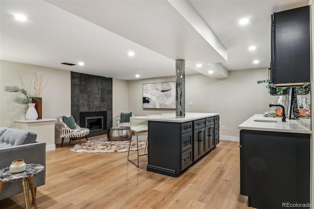 kitchen with sink, light wood-type flooring, a fireplace, a kitchen island, and a kitchen bar