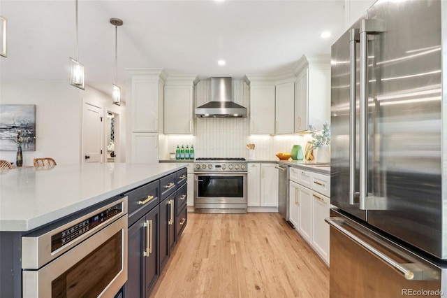 kitchen with pendant lighting, high end appliances, wall chimney exhaust hood, light hardwood / wood-style floors, and white cabinetry