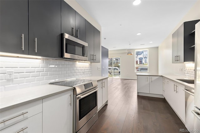 kitchen with kitchen peninsula, dark hardwood / wood-style flooring, backsplash, stainless steel appliances, and white cabinets