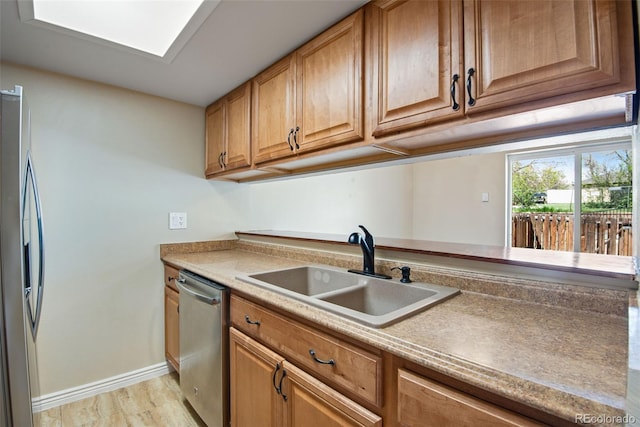 kitchen with a sink, brown cabinetry, stainless steel appliances, baseboards, and light wood-type flooring