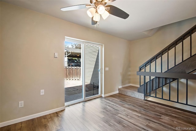 empty room featuring baseboards, ceiling fan, stairs, and wood finished floors