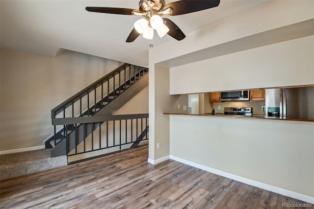 unfurnished living room featuring baseboards, a ceiling fan, stairs, and wood finished floors
