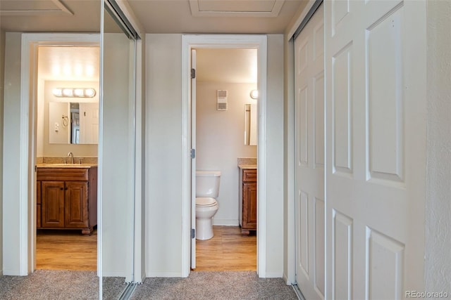 hall featuring light colored carpet, a sink, and baseboards