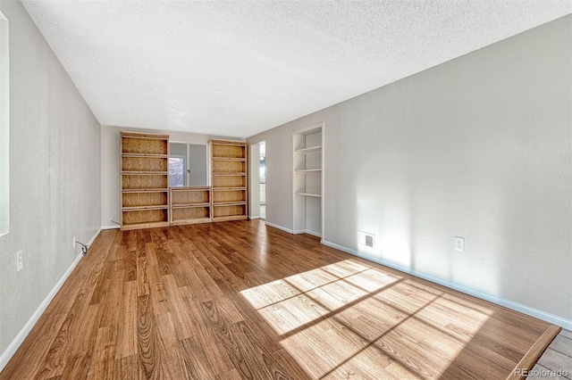 unfurnished living room with a textured ceiling, hardwood / wood-style flooring, and built in features