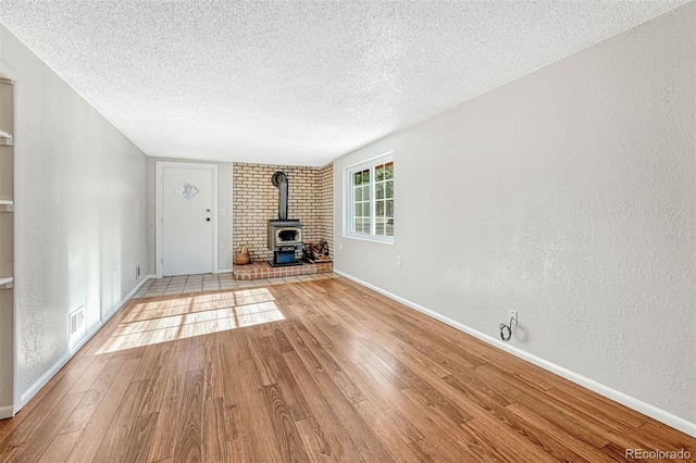 unfurnished living room with light hardwood / wood-style floors, a wood stove, and a textured ceiling