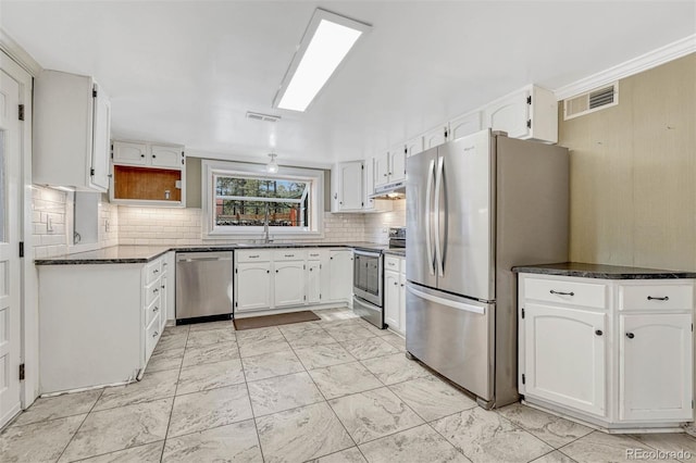 kitchen featuring white cabinetry, sink, tasteful backsplash, dark stone counters, and appliances with stainless steel finishes